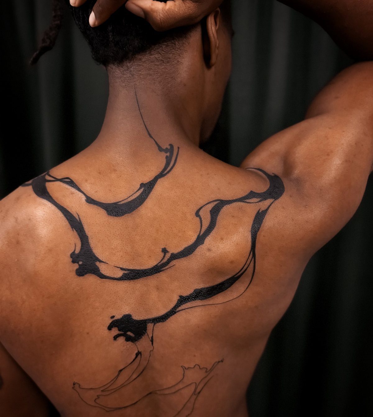 Abstract black ink tattoo with fluid flowing lines on a person's back