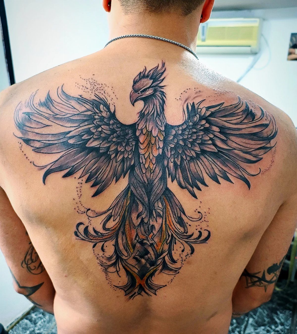 Phoenix tattoo covering a man's full back with detailed wings and orange accents.