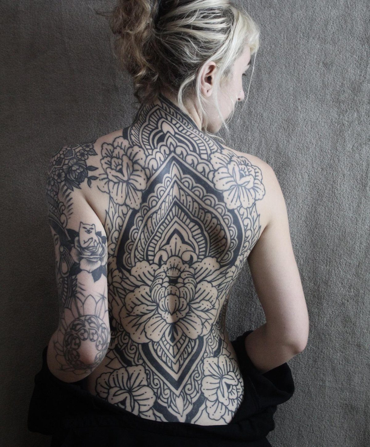 Woman with a large, symmetrical black ink floral mandala tattoo covering her entire back.