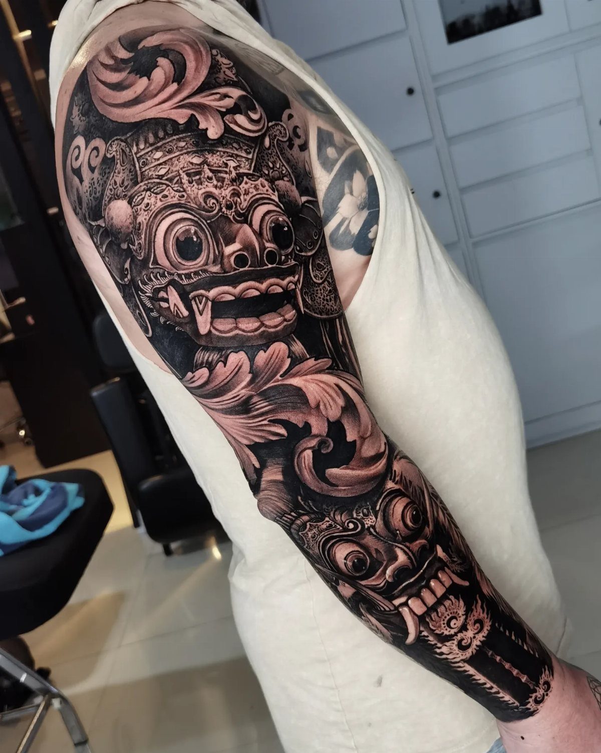 Full sleeve tattoo on a man's arm featuring detailed Balinese masks and floral patterns.