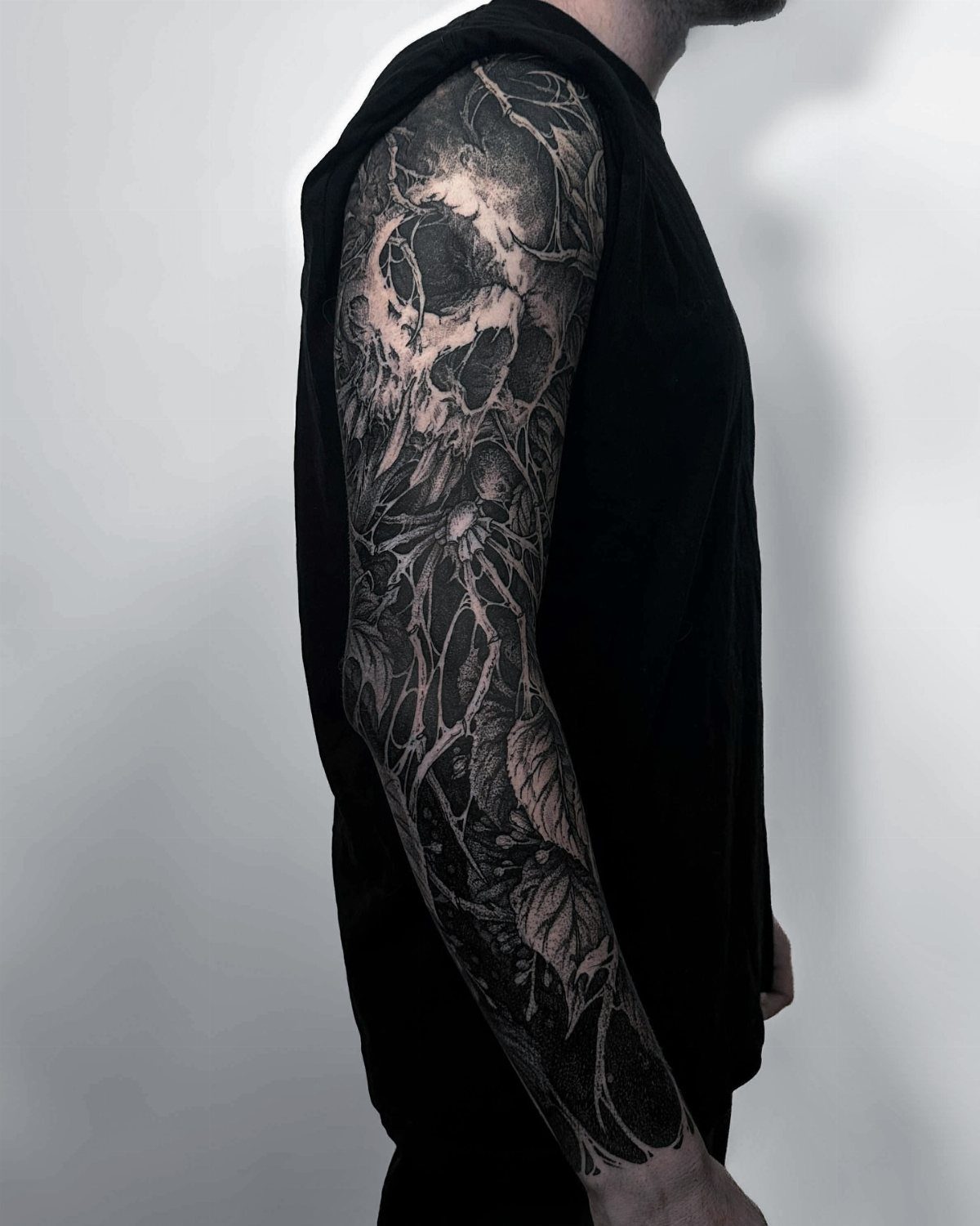 Man's arm with a bold blackwork full sleeve tattoo featuring a skull design.