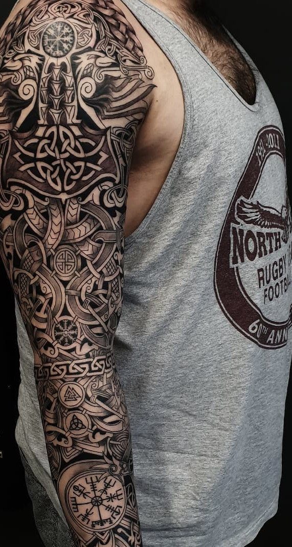 Man's arm with a full sleeve tattoo featuring intricate Celtic knots and Norse symbols.