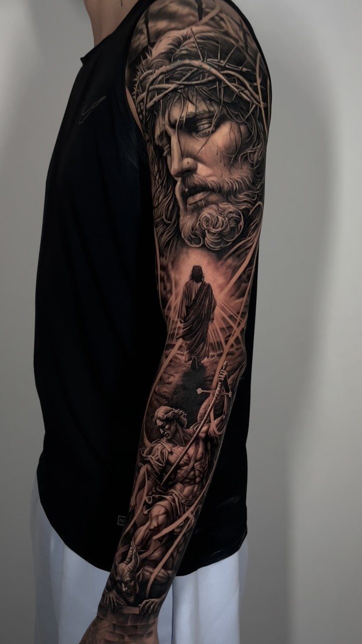 Full sleeve tattoo of Jesus with a crown of thorns on a man's arm