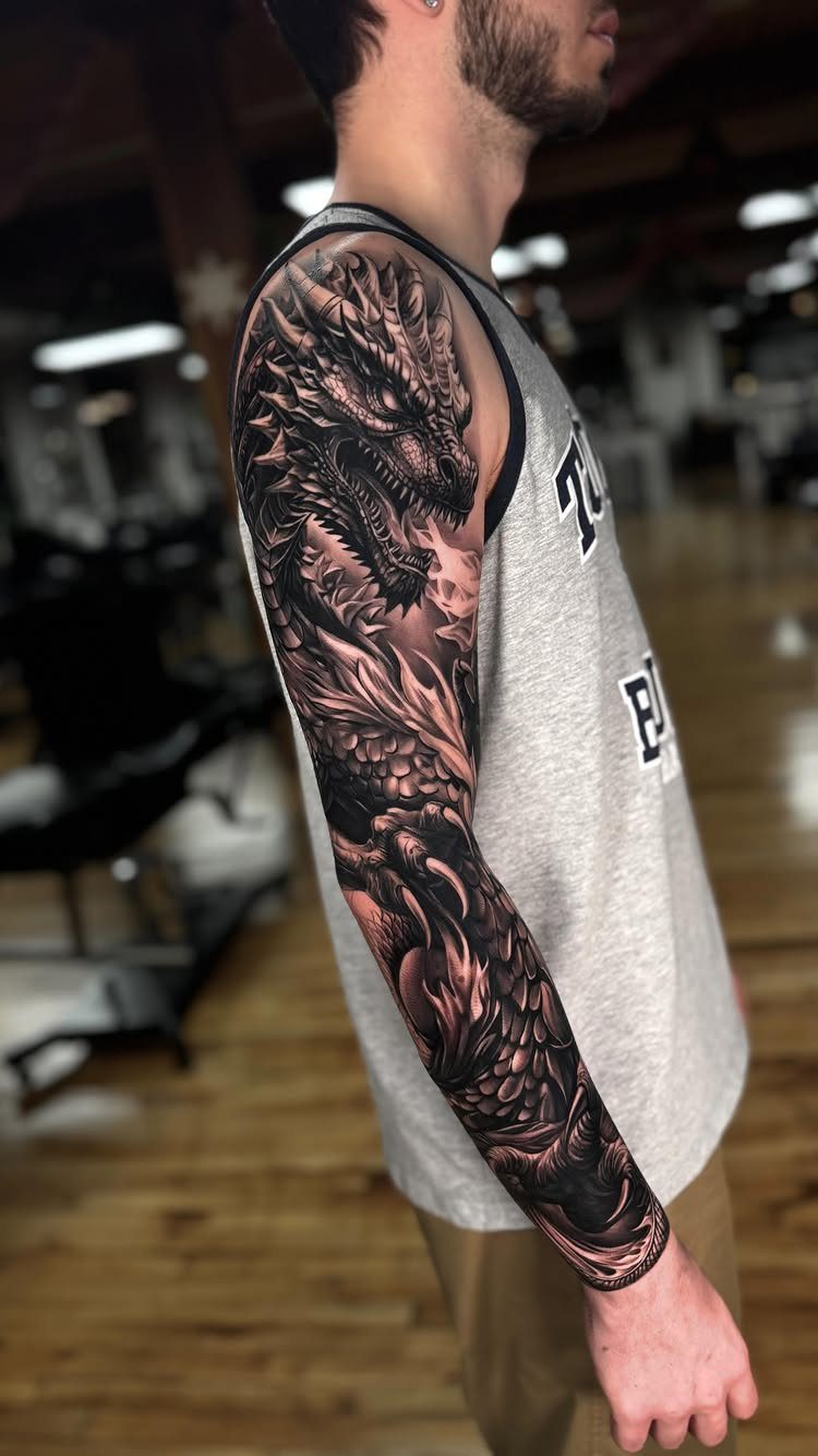 Man's arm with a detailed black and grey dragon full sleeve tattoo