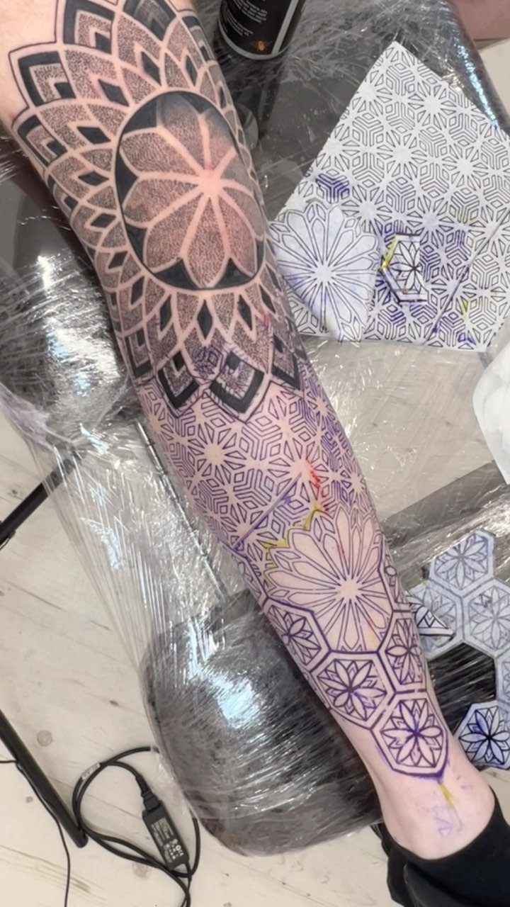 Man's arm with a full sleeve tattoo featuring complex black geometric patterns and mandalas.