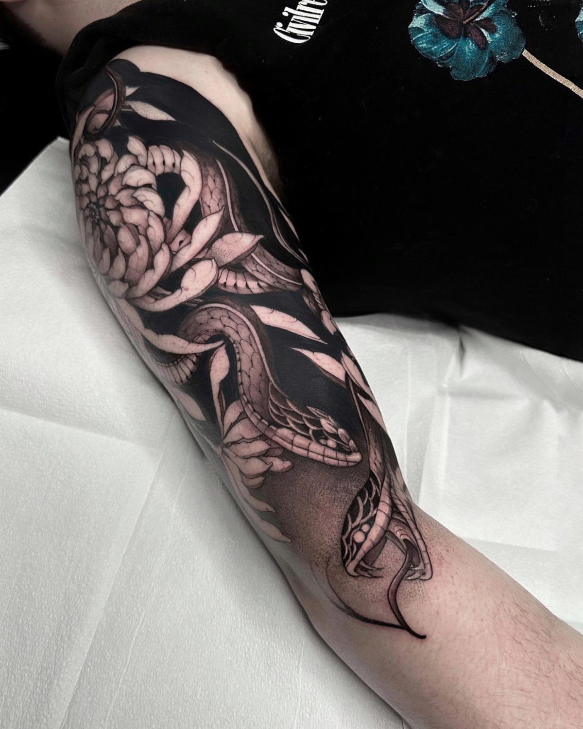 Man's arm with a black and grey half sleeve tattoo of a snake and flowers