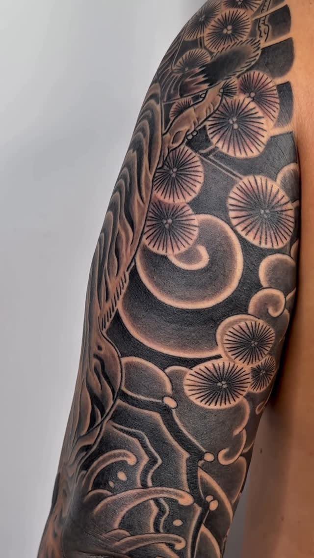 Full sleeve tattoo on a man's arm with Japanese chrysanthemums and swirling clouds