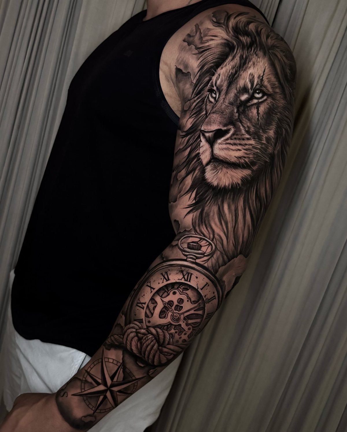 Full sleeve tattoo on a man's arm featuring a lion, pocket watch, and compass.