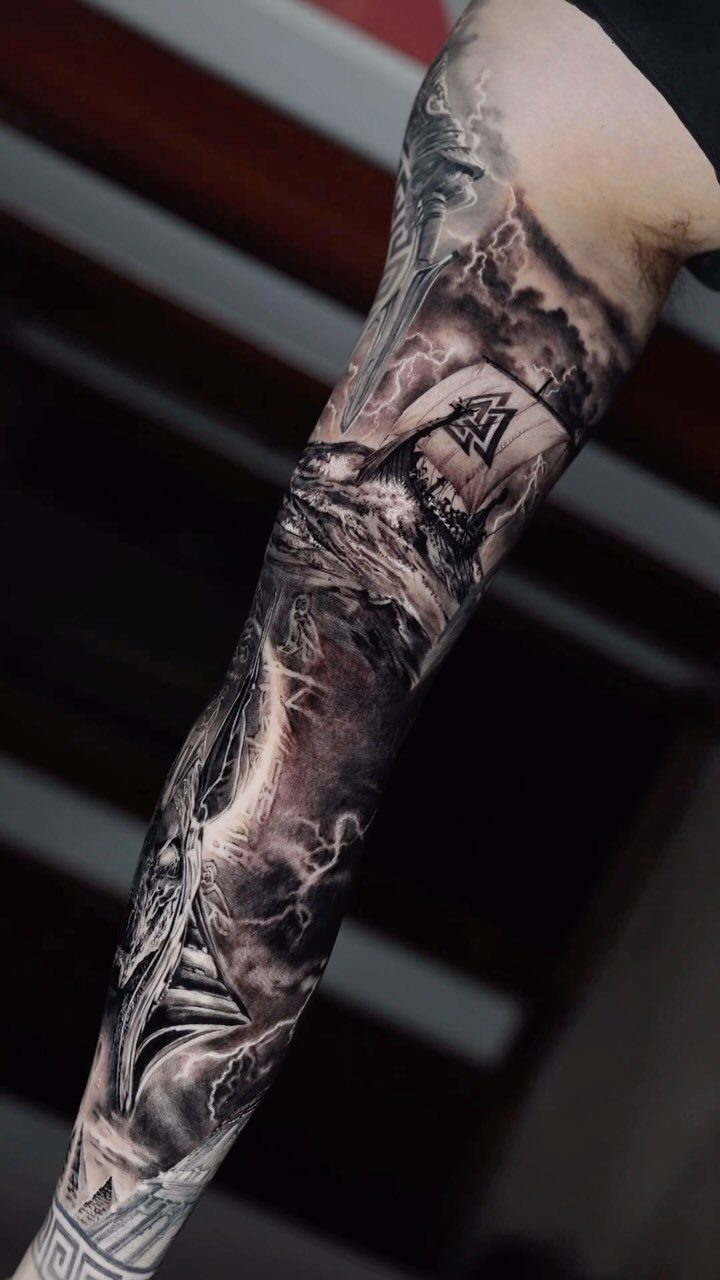 Full sleeve tattoo on arm featuring Nordic symbols, lightning, and realistic grey shading.