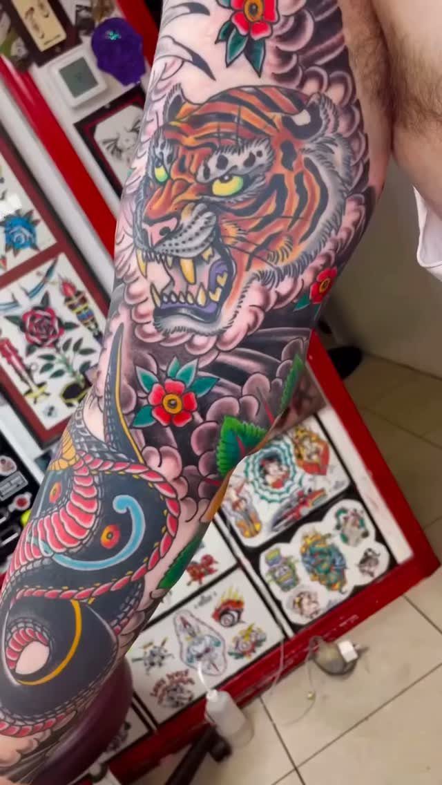 Full sleeve tattoo on a man's arm featuring a bold orange tiger and flowers.