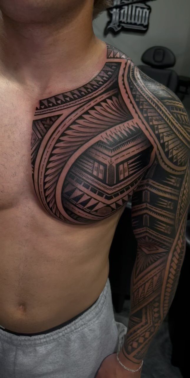Man with a bold black ink tribal tattoo covering his arm and chest