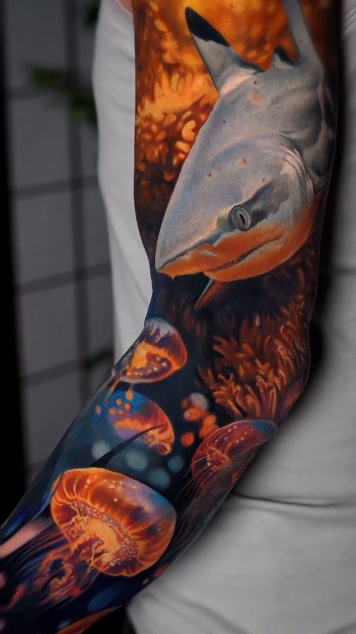 Full sleeve tattoo featuring a realistic shark and glowing orange jellyfish.