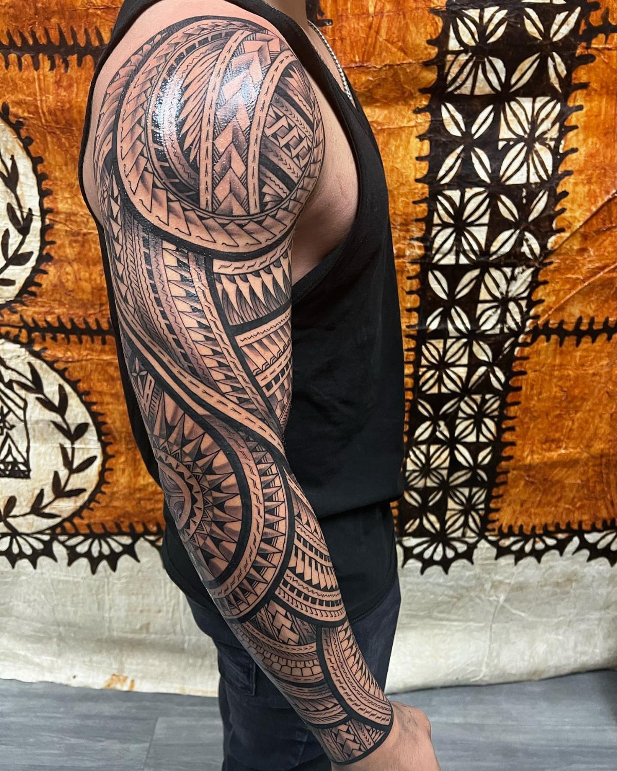 Full sleeve tribal tattoo with black geometric patterns on a person's arm.