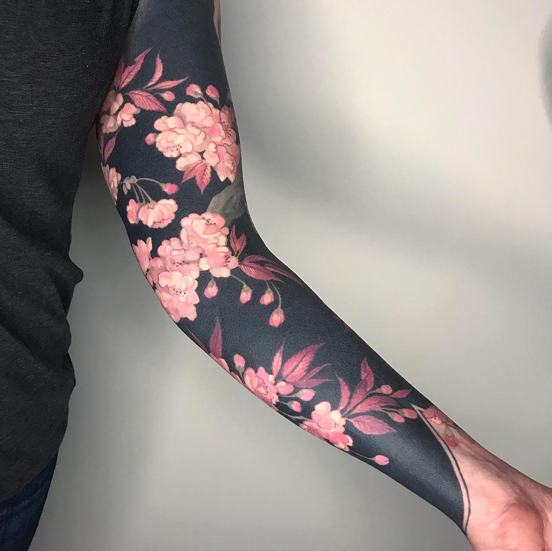 Full sleeve tattoo with pink cherry blossoms on a dark shaded arm background.