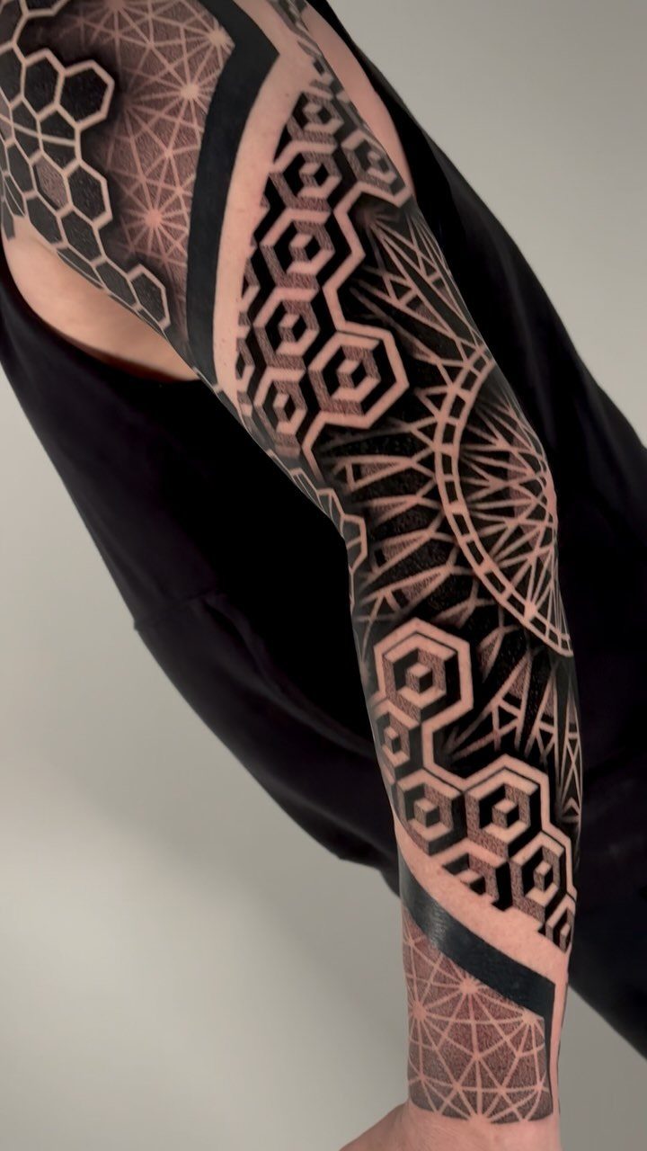 Geometric sleeve tattoo with black ink hexagons and intricate symmetrical patterns on an arm.