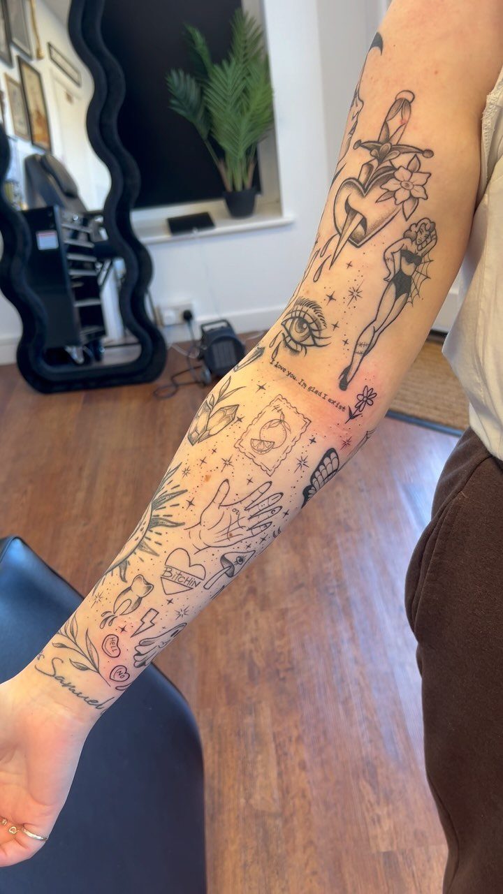 Arm with a patchwork sleeve tattoo featuring various small, unrelated black ink designs.