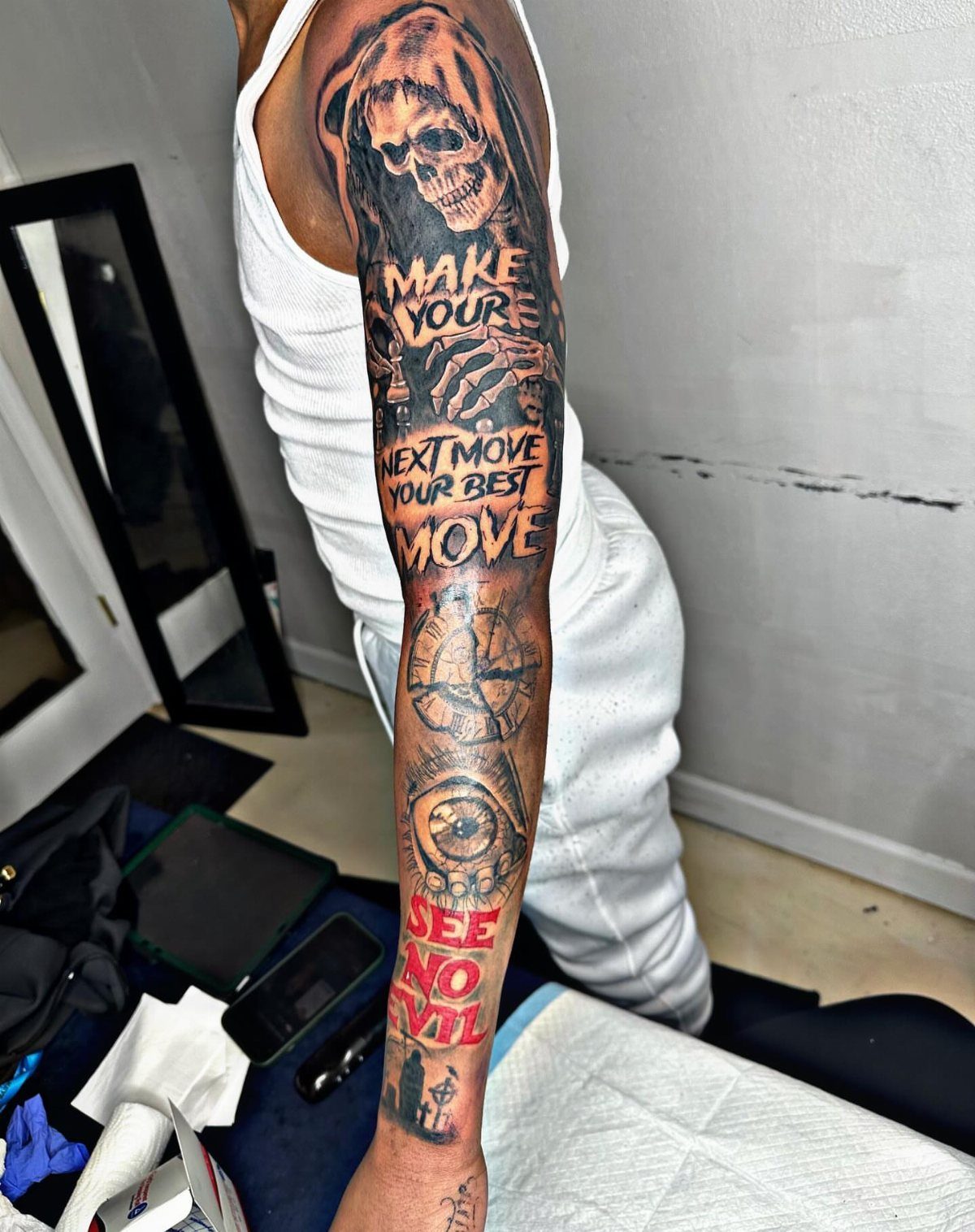 Full sleeve tattoo featuring a skull, compass, clock, and motivational text on an arm.