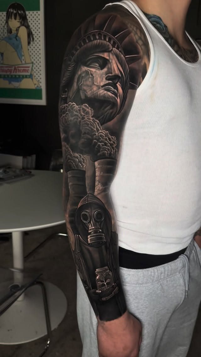 Full sleeve tattoo on an arm featuring the Statue of Liberty and a gas mask.