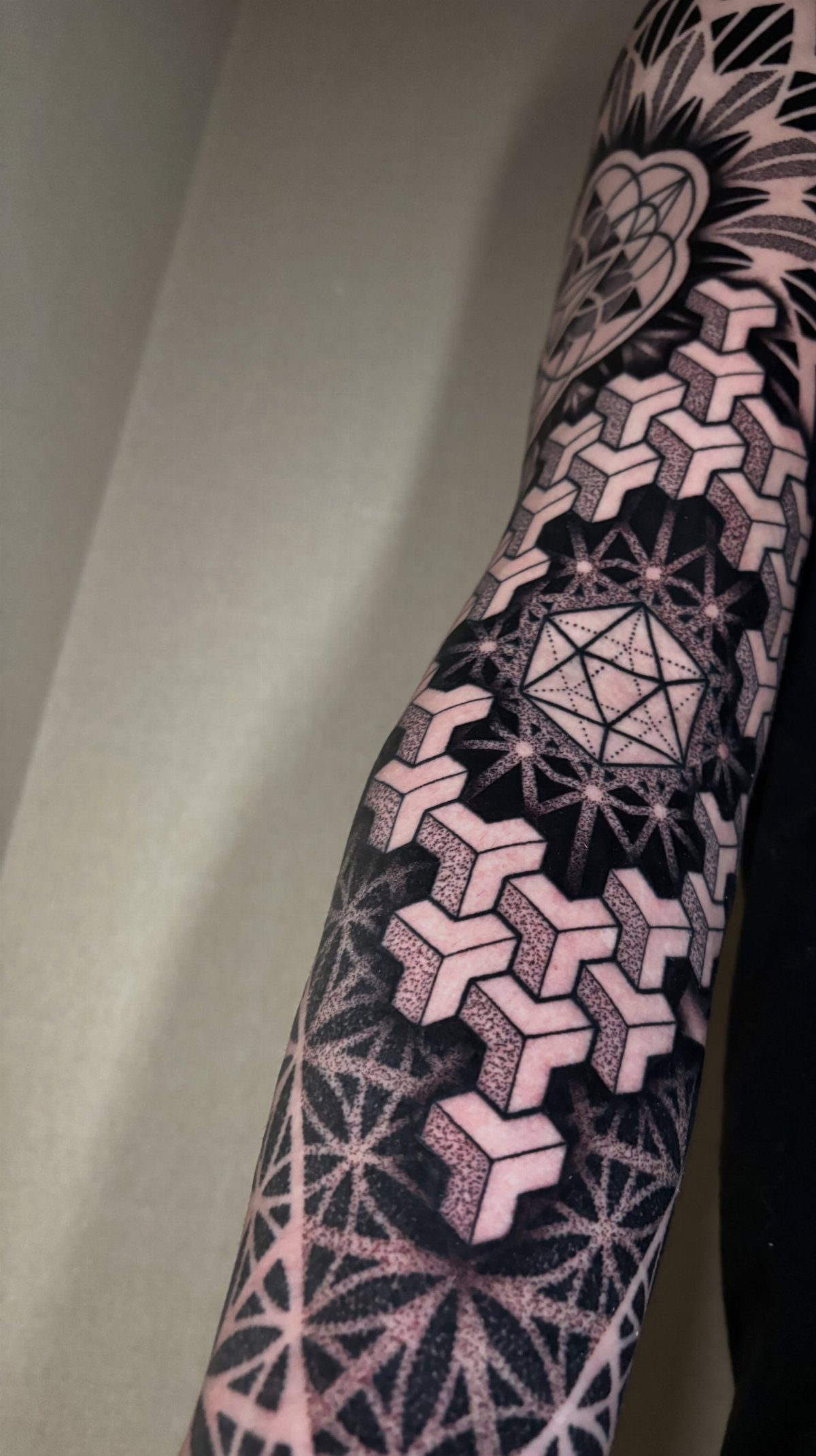 Geometric tattoo on an arm featuring an icosahedron and 3D cubic patterns.