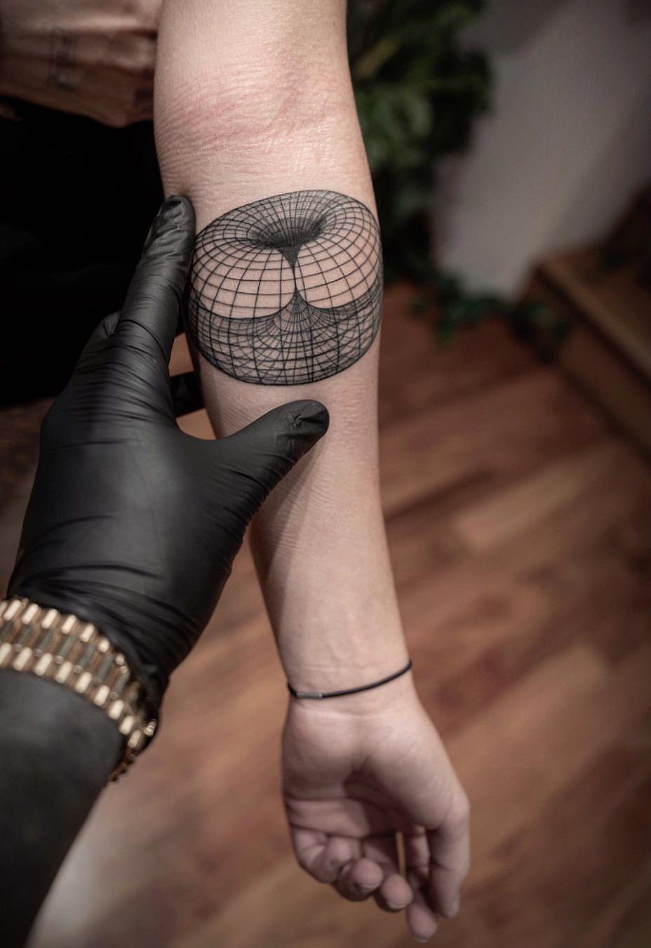 Geometric spherical grid tattoo on a forearm being pointed to by a gloved hand.