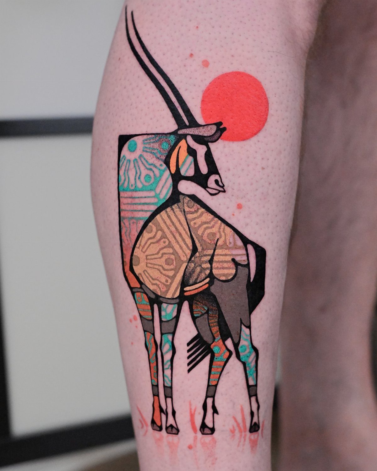 Geometric oryx tattoo with colorful patterns and a red sun on an arm