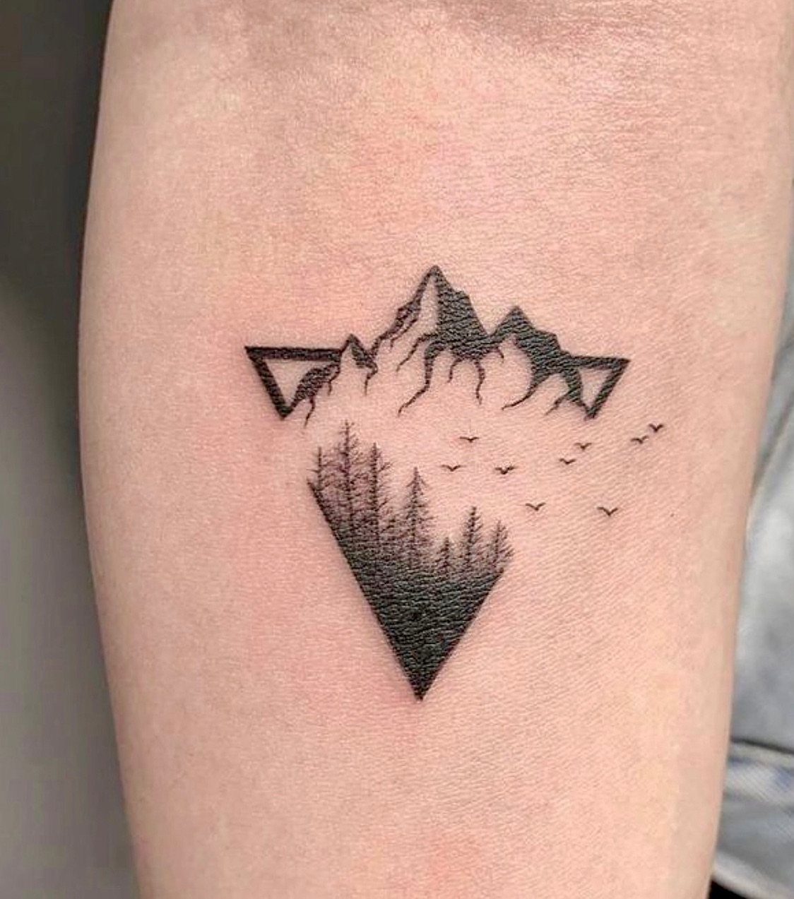 Geometric tattoo of a mountain range and pine forest inside a diamond frame.