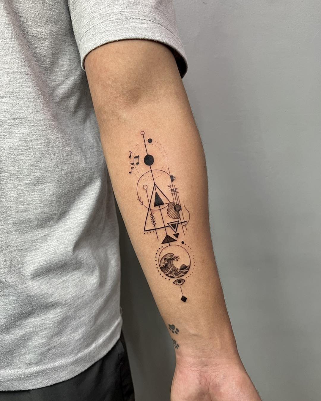 Forearm with a black ink geometric tattoo featuring circles, triangles, and a wave.