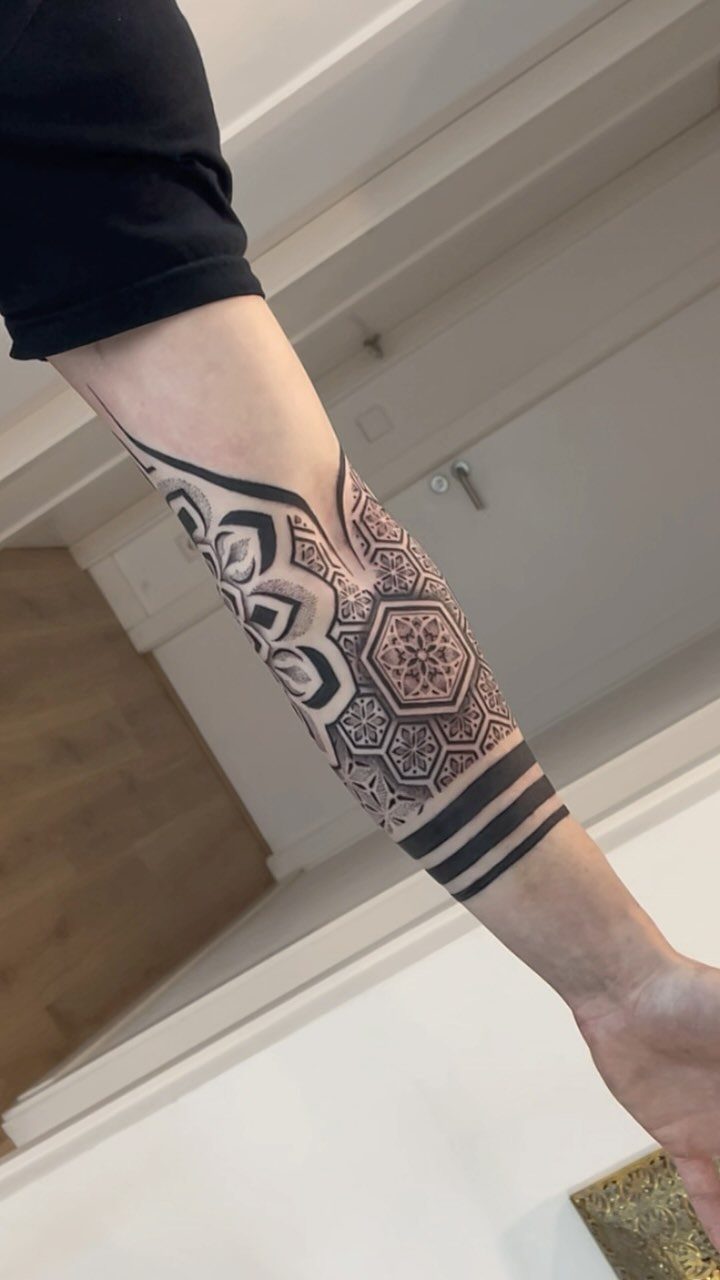 Forearm tattoo combining a detailed mandala design with sharp geometric patterns and black bands.