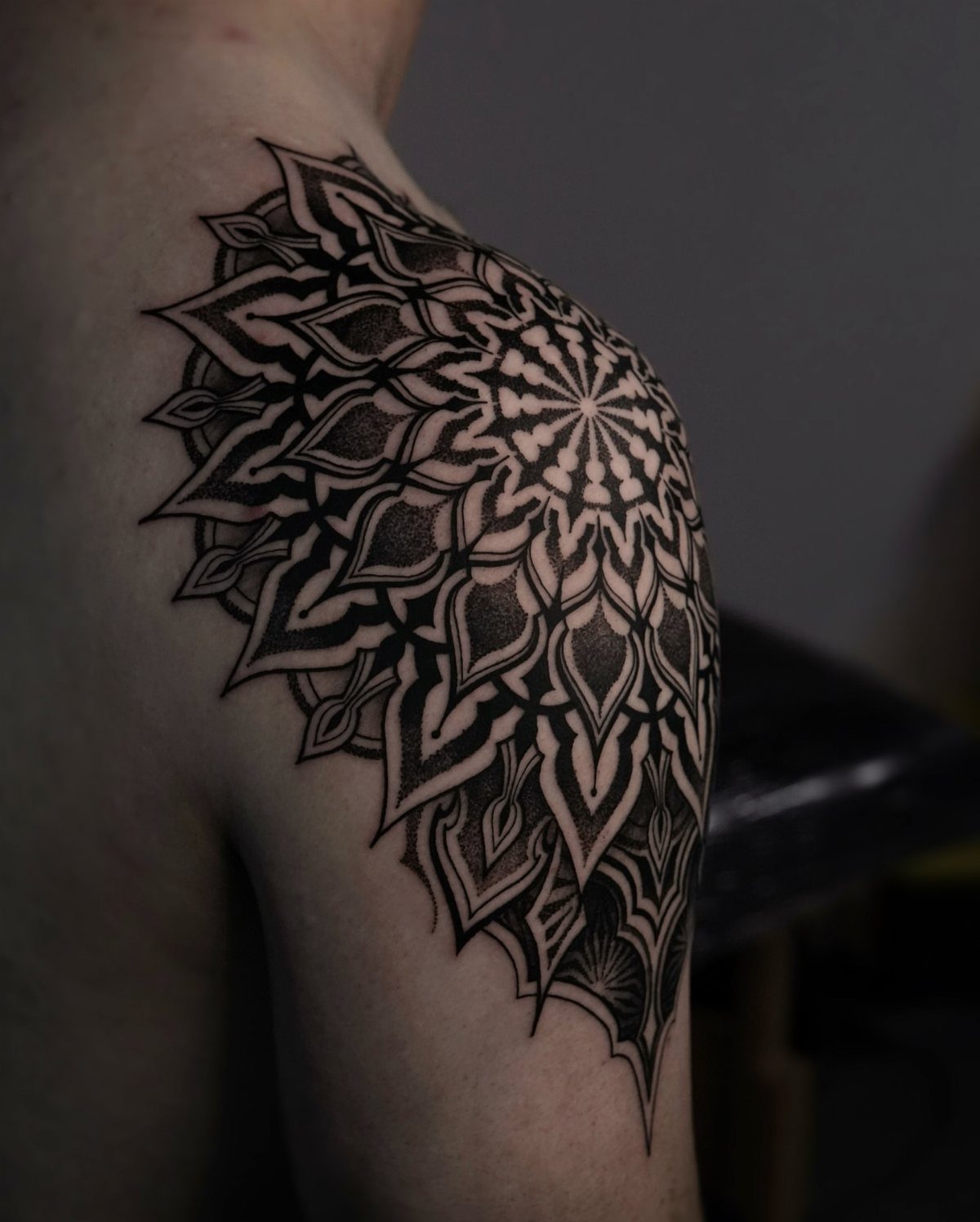 Mandala tattoo with intricate black geometric patterns covering a man's shoulder and upper arm.