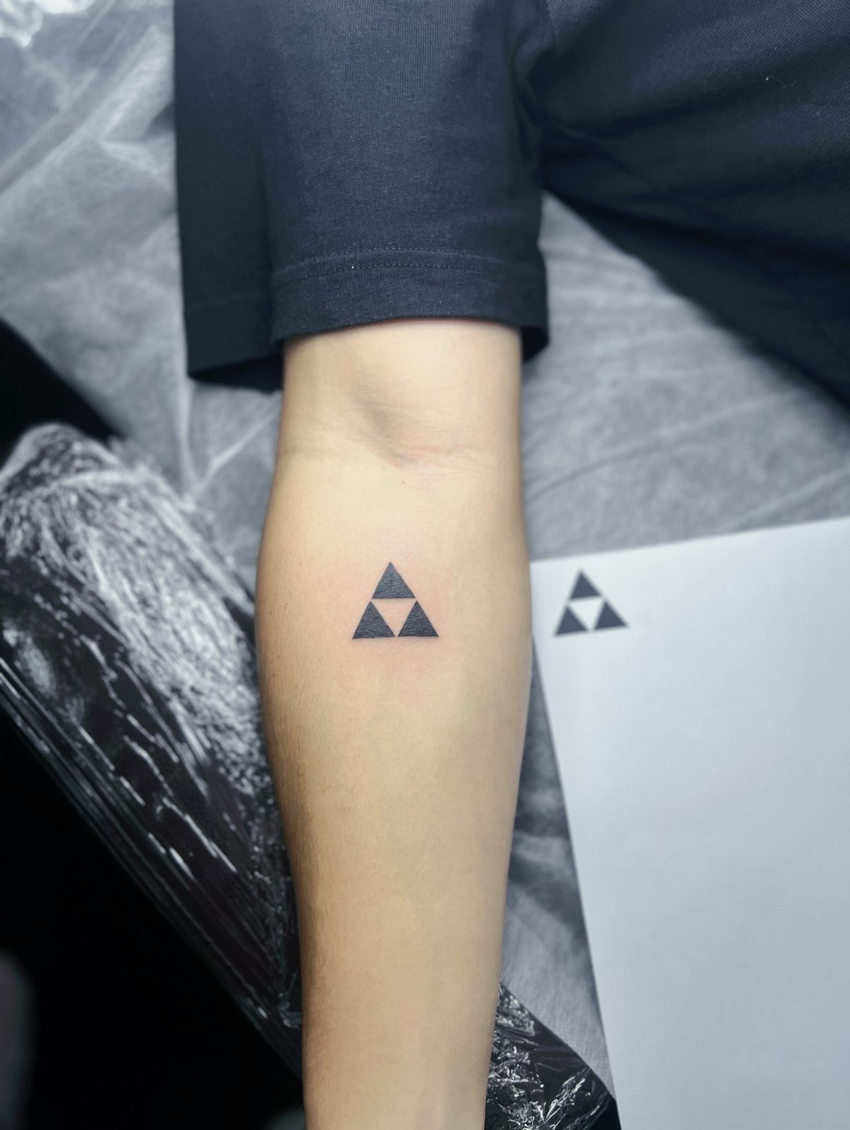 Minimalist black triangle tattoo on a person's forearm next to a design reference.