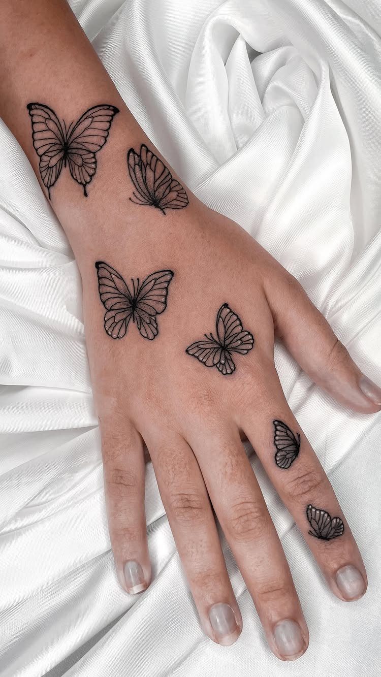 Hand and wrist with multiple black ink butterfly tattoos on a white fabric.