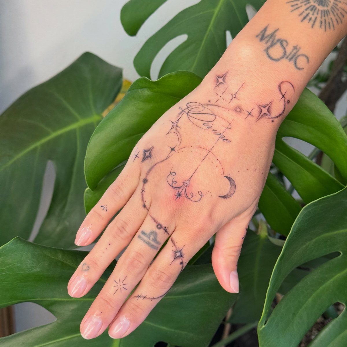 Hand with celestial tattoos including a crescent moon and stars on green leaves
