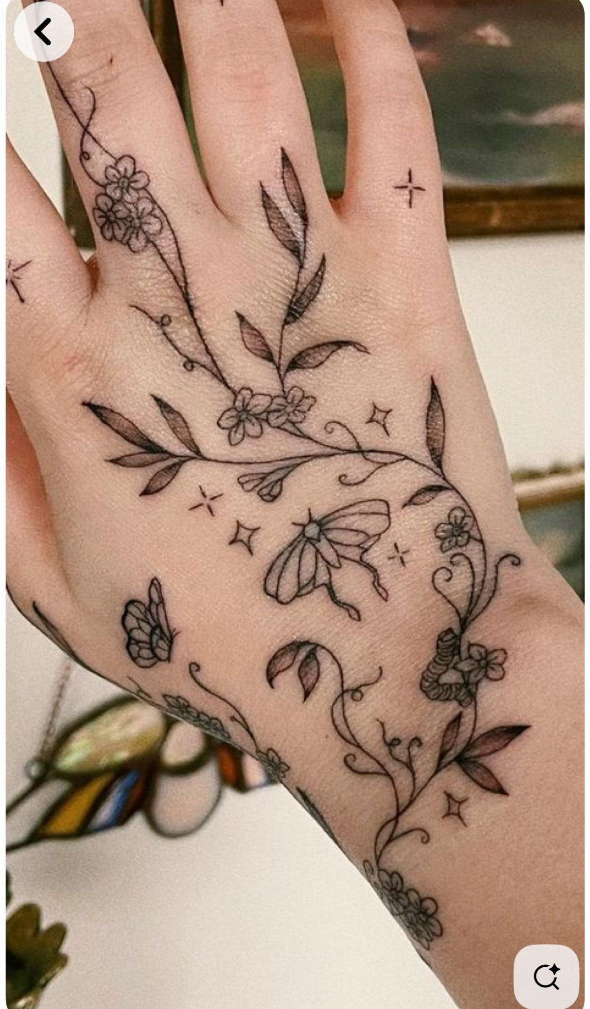 Hand with tattoos of delicate flowers, leaves, vines, and butterflies in black ink