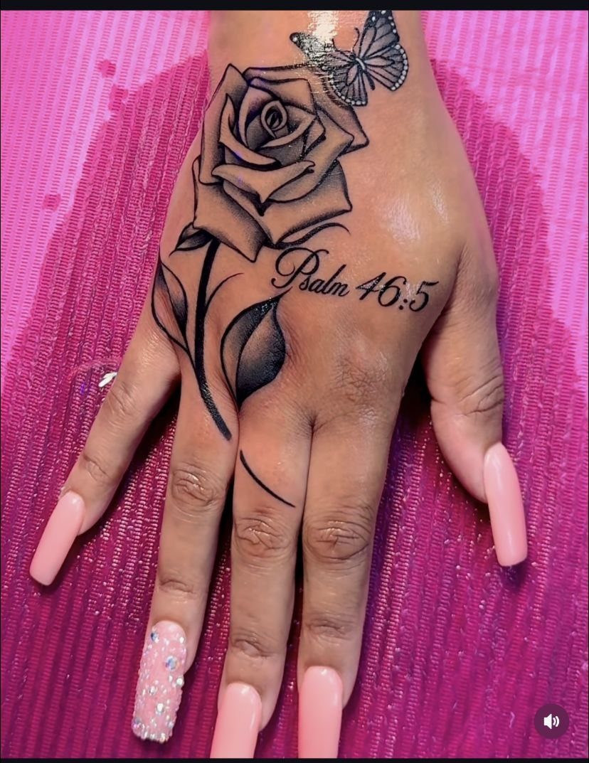 Hand with a rose and leaves tattoo, a butterfly, and biblical script.