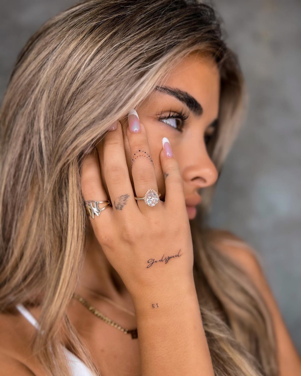 Woman's hand featuring a script tattoo on the side and rings on fingers.