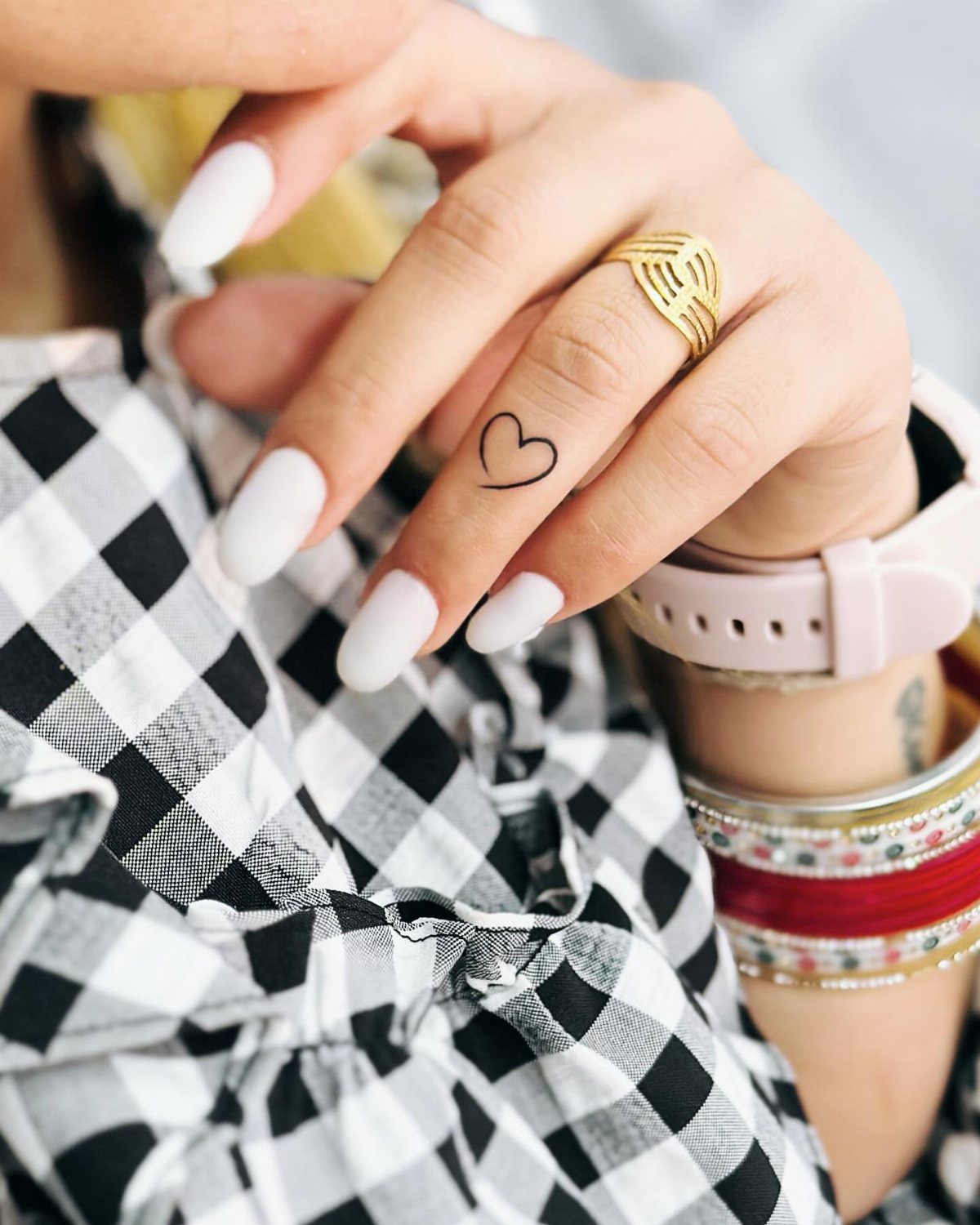 Hand with white nails and a small heart tattoo on the ring finger