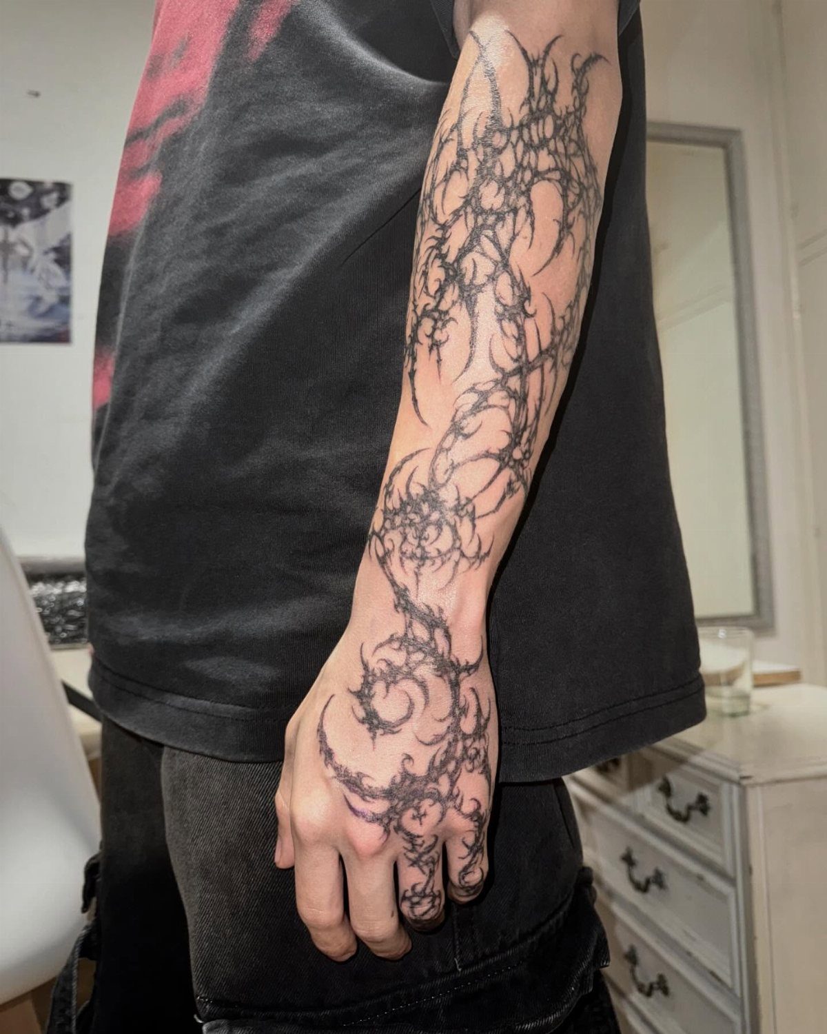 Black ink abstract thorn tattoo covering a person's arm and hand