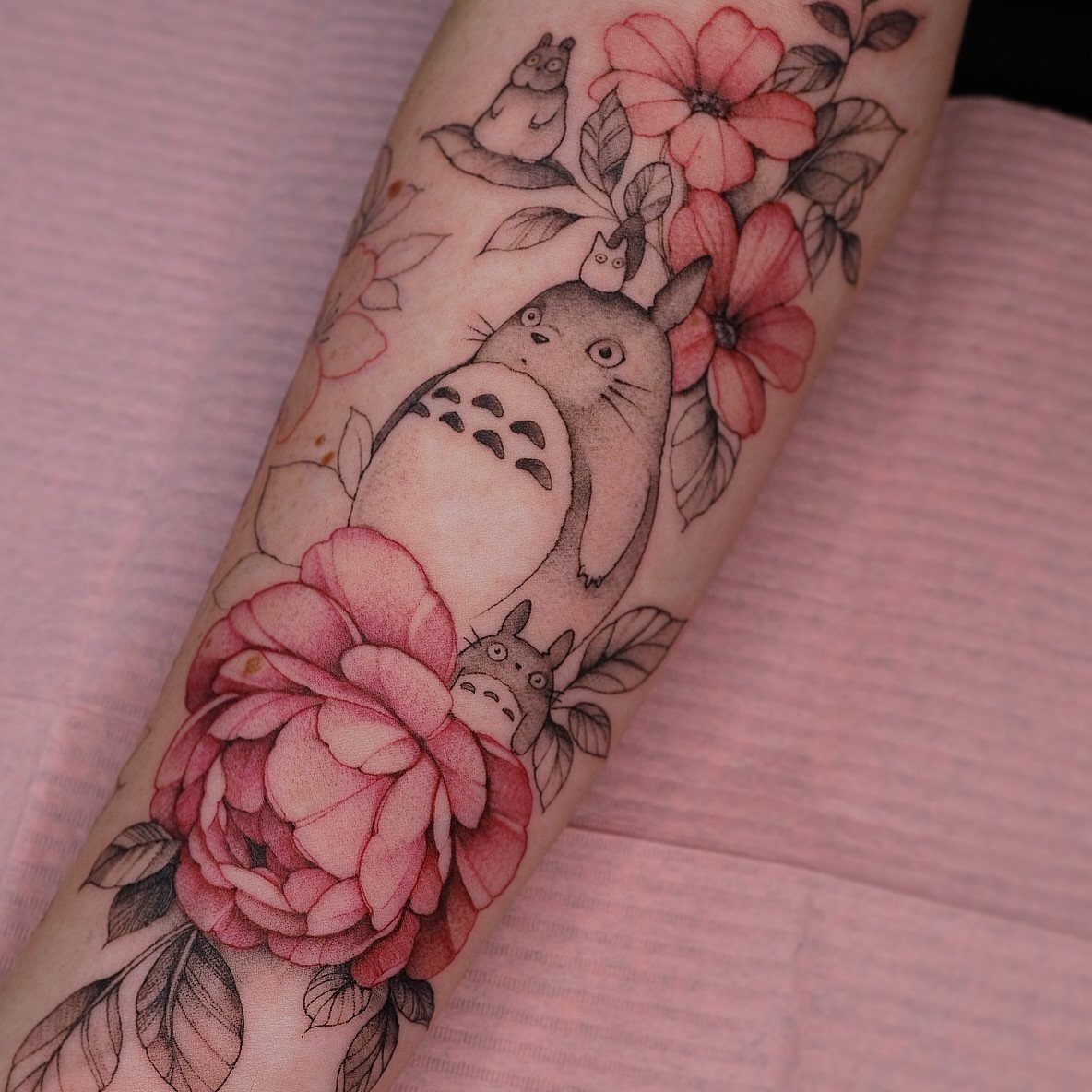 Totoro and pink flowers tattoo on a person's forearm