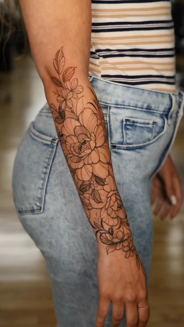 Floral half sleeve tattoo on a person's forearm with detailed black ink blossoms