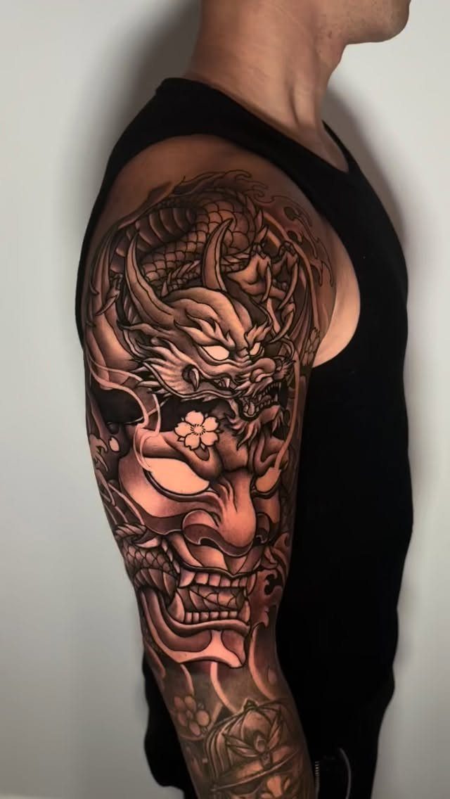 Hannya mask and dragon half sleeve tattoo on a man's upper arm.
