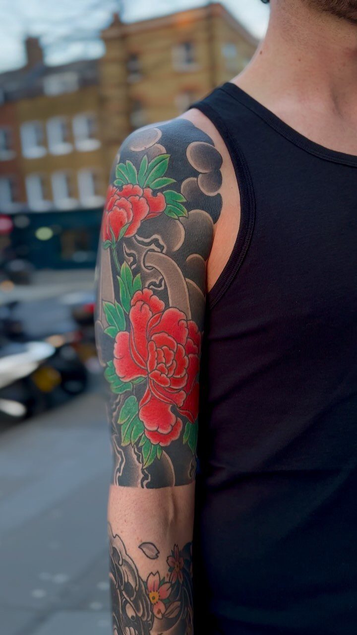 Half sleeve tattoo with red peonies and grey clouds on a person's arm