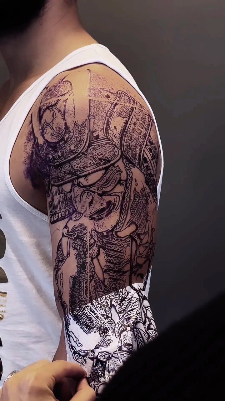 Detailed black ink samurai mask half sleeve tattoo on a person's upper arm