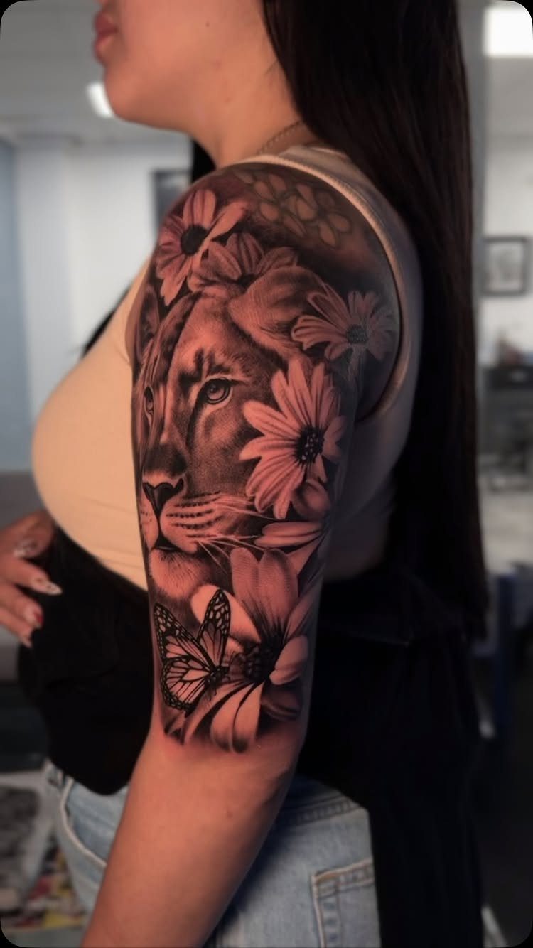 Lion face tattoo with flowers and a butterfly on a person's upper arm.