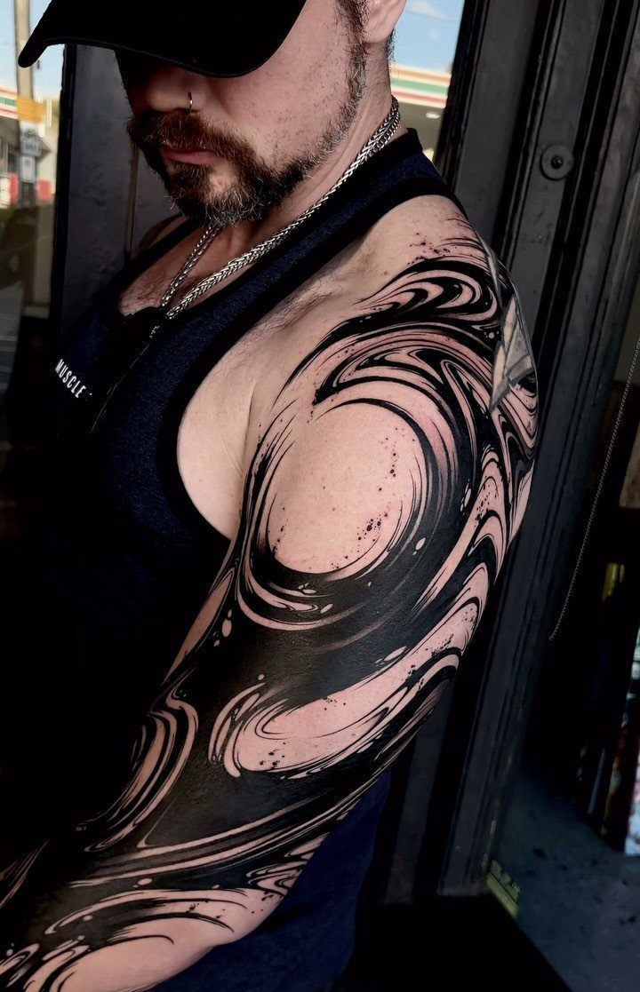Man with a black abstract swirling ink half sleeve tattoo on his arm.