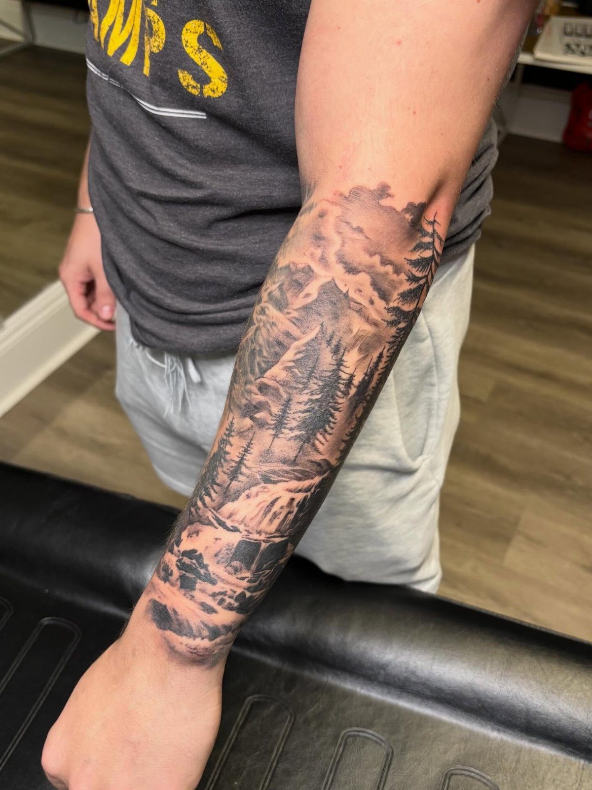 Forest and mountain landscape half sleeve tattoo on a man's forearm in black and grey.