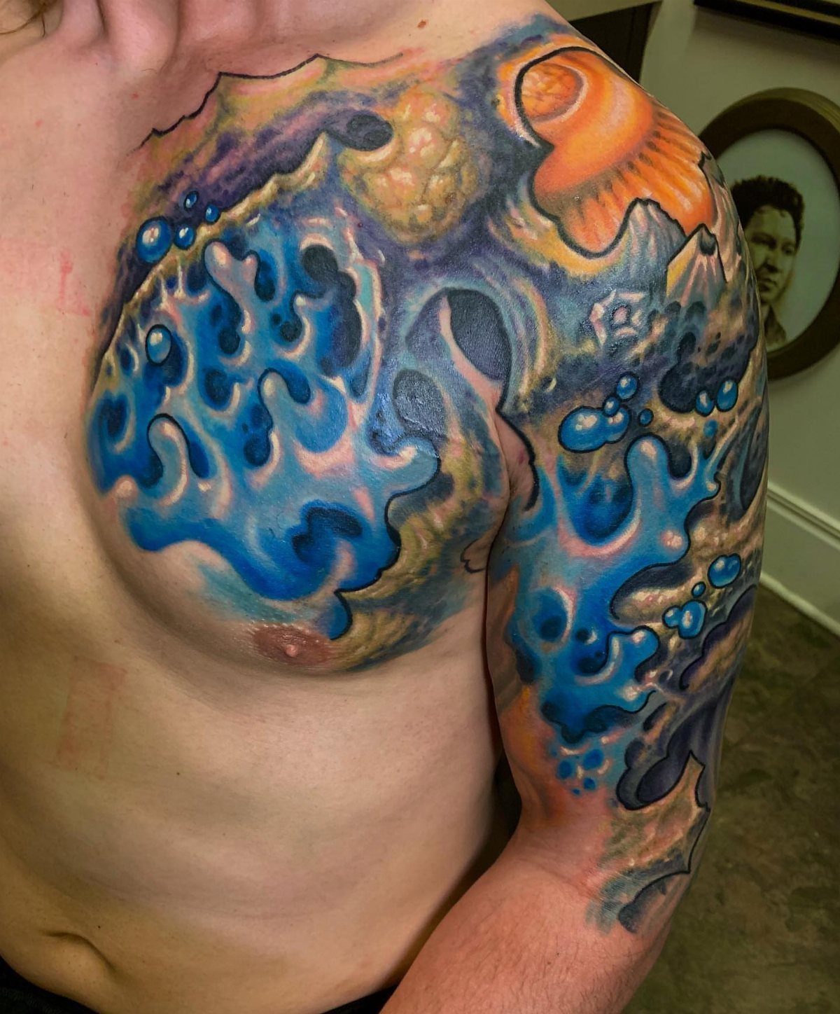 Colorful oceanic tattoo with blue water and orange coral on a man's arm.