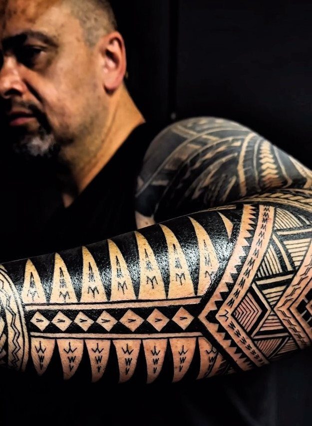 Polynesian tribal tattoo with black geometric patterns on a man's muscular upper arm.