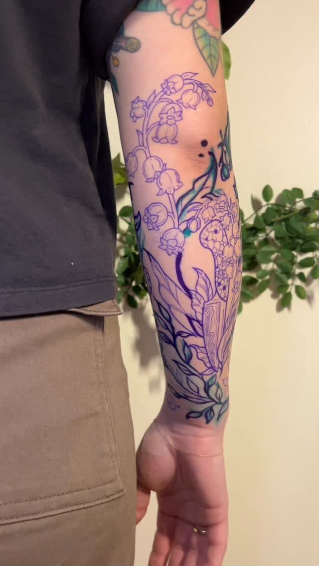 Forearm with a detailed purple and blue floral half sleeve tattoo.