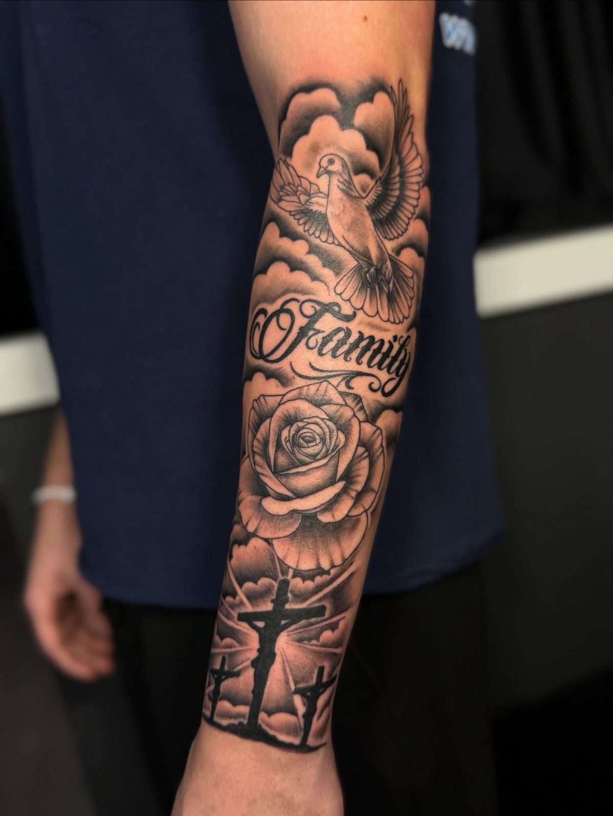Forearm half sleeve tattoo with a dove, rose, crosses, and Family script.