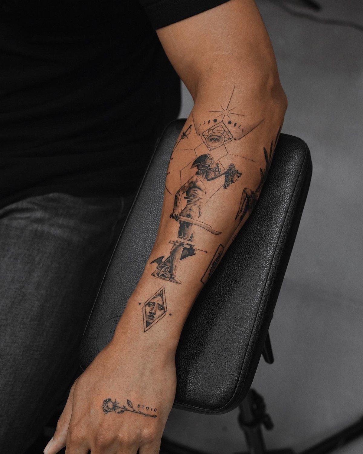 Forearm tattoo featuring a central figure surrounded by precise geometric lines and shapes.